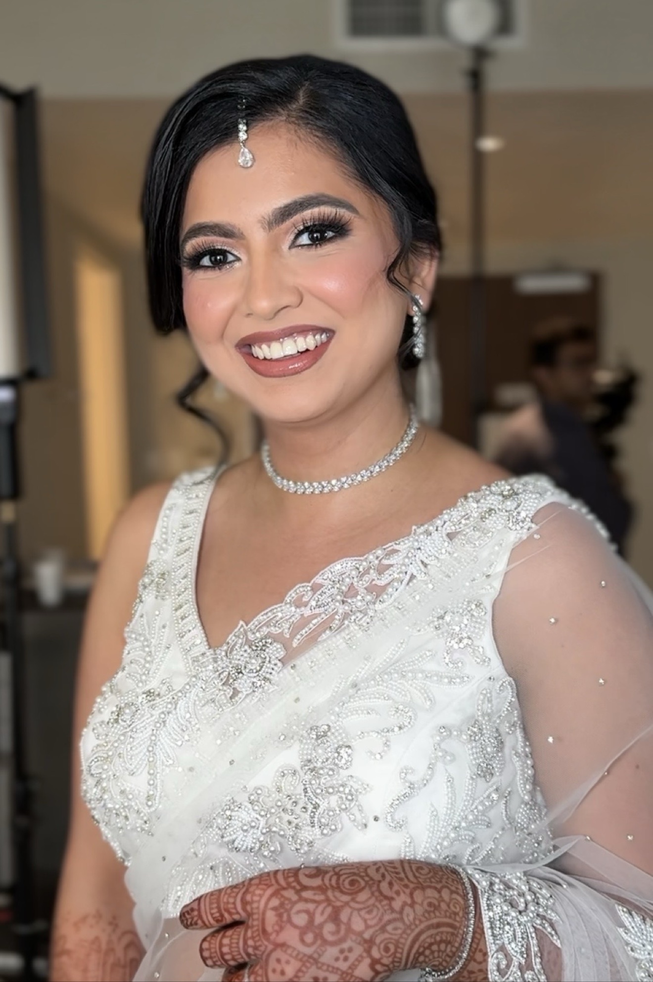 Smiling bride in white embroidered outfit with henna hand and diamond jewelry, JTorry Makeup + Hair Artistry