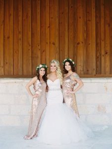 Western bride in white strapless gown posing with two bridesmaids in gold sequin dresses and floral crowns